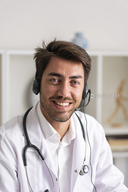 年轻英俊的男医生戴着无线耳机说话，用笔记本电脑