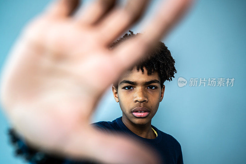 一个男孩在蓝色背景上做停止手势的肖像