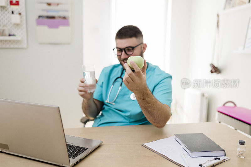 医生在办公室用笔记本电脑，喝水，吃苹果