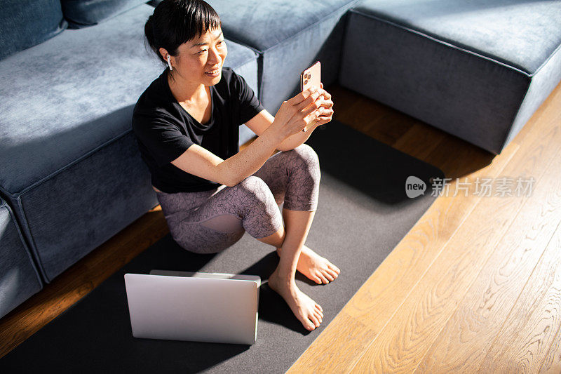 年轻的日本女子在家里锻炼后使用智能手机