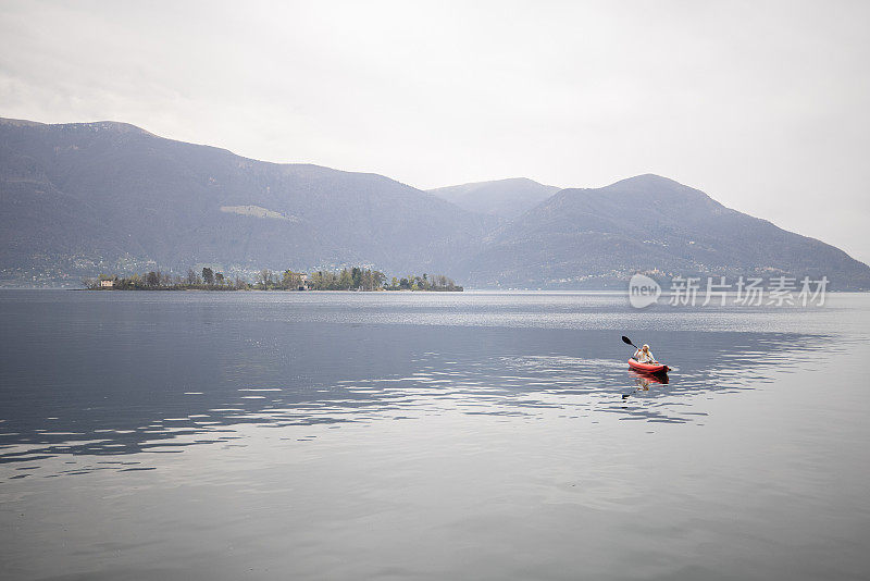 远处的人在阴天平静的湖面上划独木舟