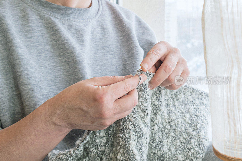 一个女人正在织一条灰色的羊毛围巾。这个女人正在做针线活。