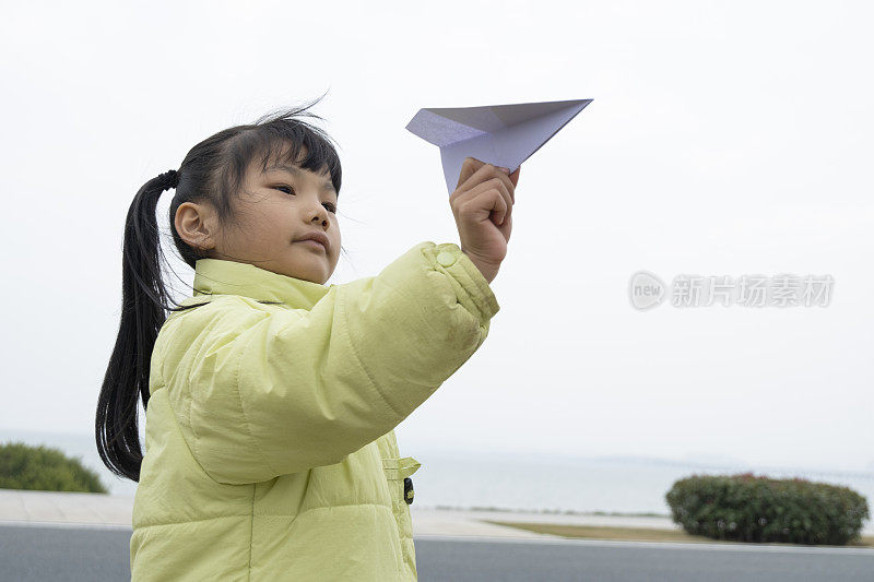 穿着浅绿色衣服的亚洲小女孩在玩纸飞机