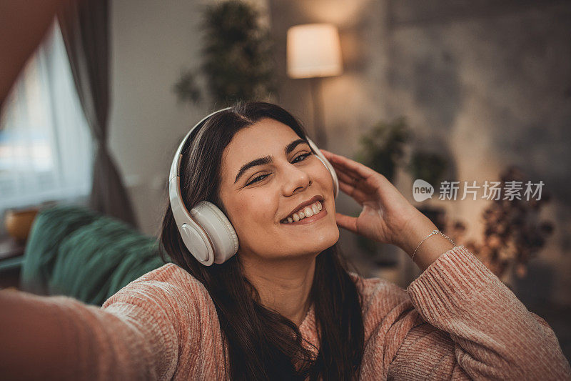 一个女人，一个漂亮的年轻女人在家里戴着耳机听音乐，听着她最喜欢的播放列表