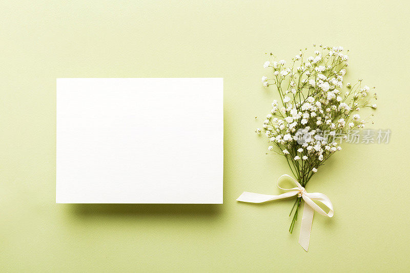 婚礼模型与白色的纸清单和鲜花石膏在彩色的桌面视图平躺。空白的贺卡和信封。漂亮的花卉图案。平铺式