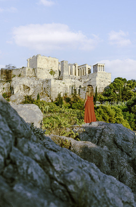 希腊雅典，日落时分，一名年轻女子在阿略帕古斯山上欣赏雅典卫城遗址的景色