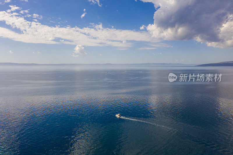 无人机航拍照片。一艘孤独的小游艇在一望无际的湛蓝透明的大海中。天空中有大片的云。在海上度假。
