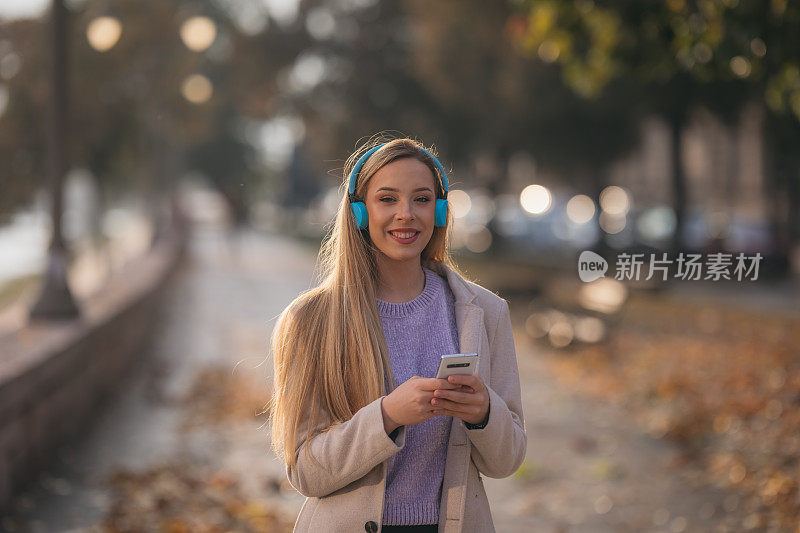 年轻的白人女子在城市里用智能手机和耳机笑得很开心