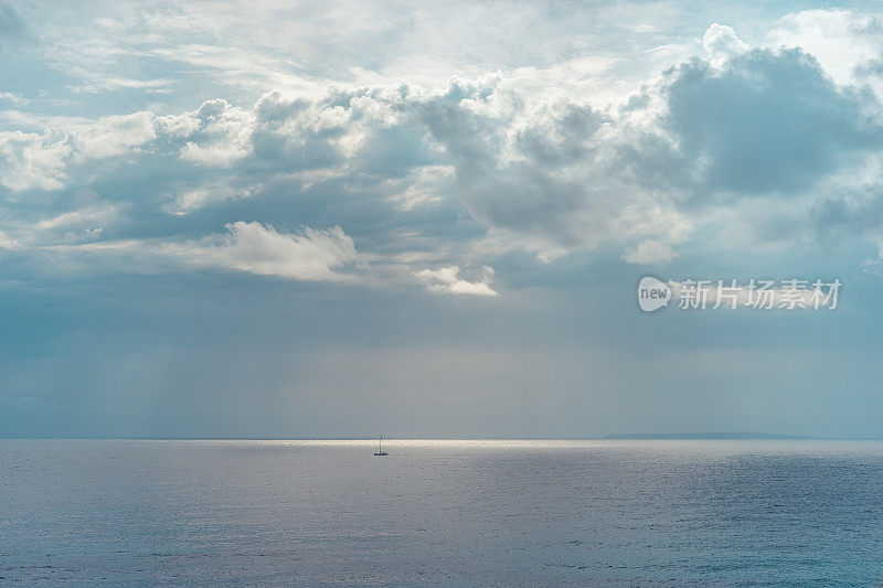 西班牙伊比沙岛，一艘船在充满威胁的云层和光束的戏剧性天空下航行