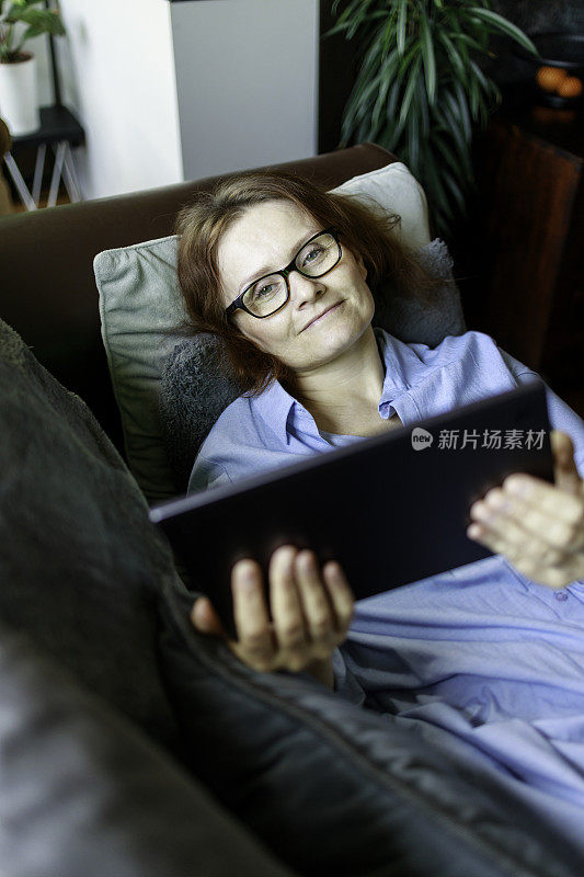 一个女人躺在家里的沙发上用平板电脑