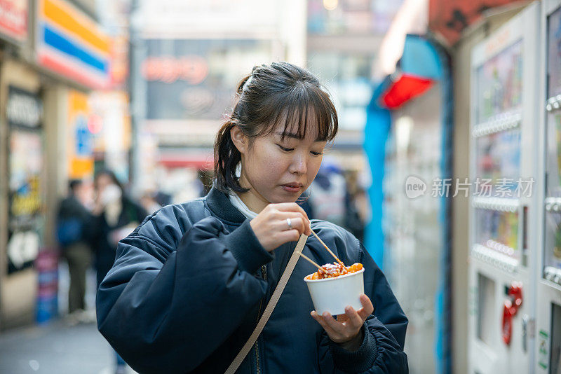 年轻女游客在街上吃韩国小吃