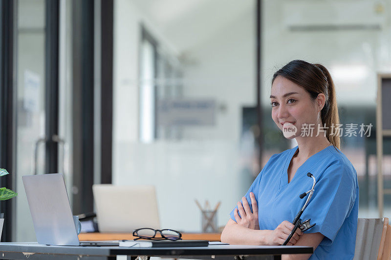 微笑的成年女医生在一个蓝色制服听诊器，抱着双臂，一个自信的女医生看向别处。