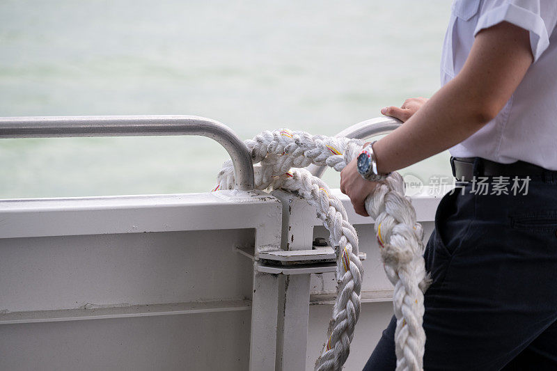 船上的女性双手握着绳子，准备把船系到港口。选择性地关注绳子。