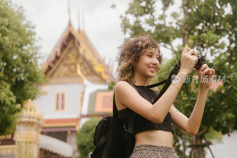 有魅力的年轻女游客夏天背包旅行，在步行街享受户外生活和拍照。