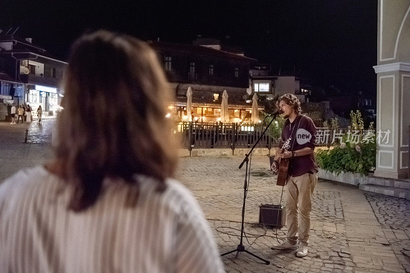 深夜，街头艺人在街上唱着歌，弹着吉他。