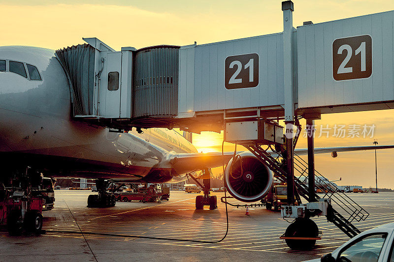 现代客机在机场的空侧停机坪停在航站楼门口，近距离观察飞机部件，喷气发动机，机翼，窗户，齿轮，牵引车，正午的阳光视野