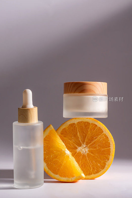 含有维生素C的柑橘类化妆品和灰色背景上的橙子片。用滴瓶和面霜瓶装的面部精华液。设计空白包装