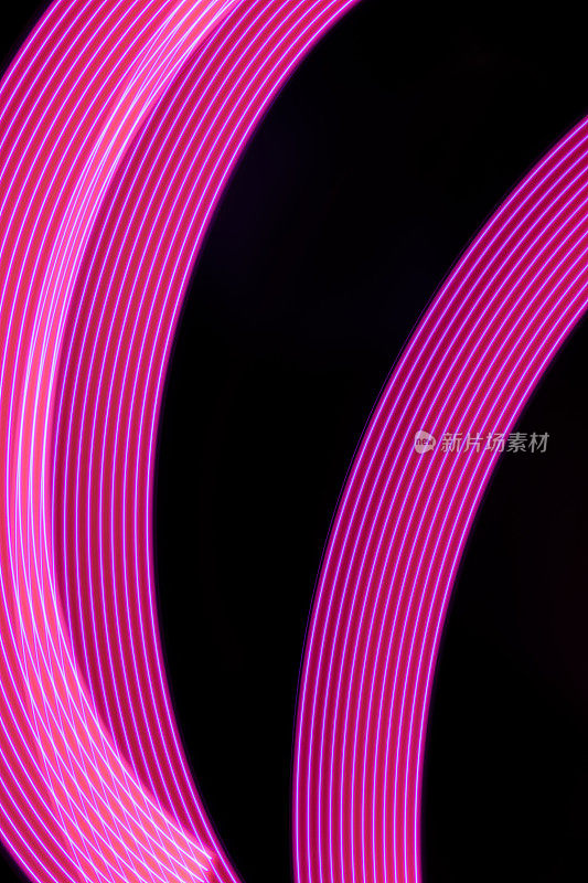 粉红色和紫色的霓虹灯弯曲的线条与平滑的条纹在黑色的背景，垂直。抽象的背景与运动灯光效果，灯光绘画在节日的风格。