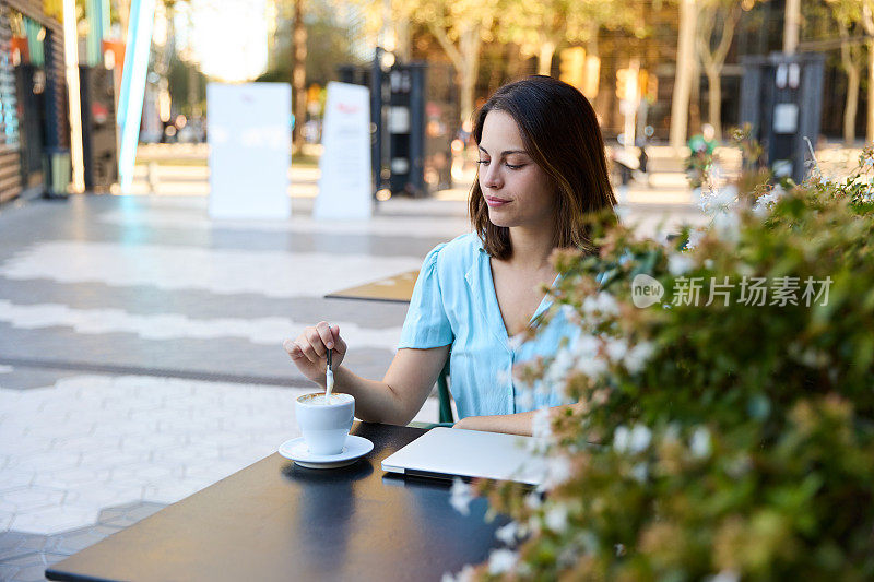 宁静的女商人在城市的户外咖啡馆里搅拌咖啡