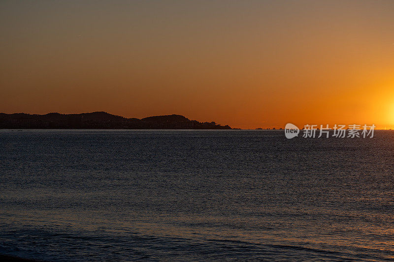Palamós海岸和渔船被地中海地平线上黎明的太阳微妙地照亮，从港口出海捕捉虾，平静的海水被橙色的色调照亮