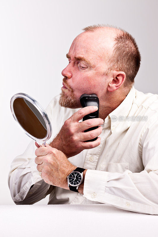 用电动剃须刀刮胡子的成熟男子在镜子前检查