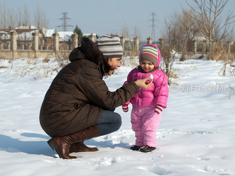 妈妈和美丽的蹒跚学步的女孩在雪中玩耍