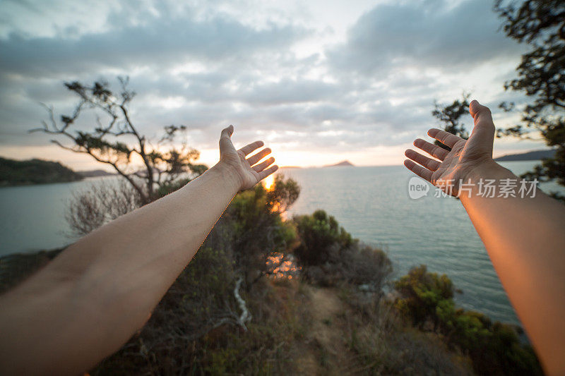 在新西兰豪拉基湾，一个女人的手臂伸向夕阳