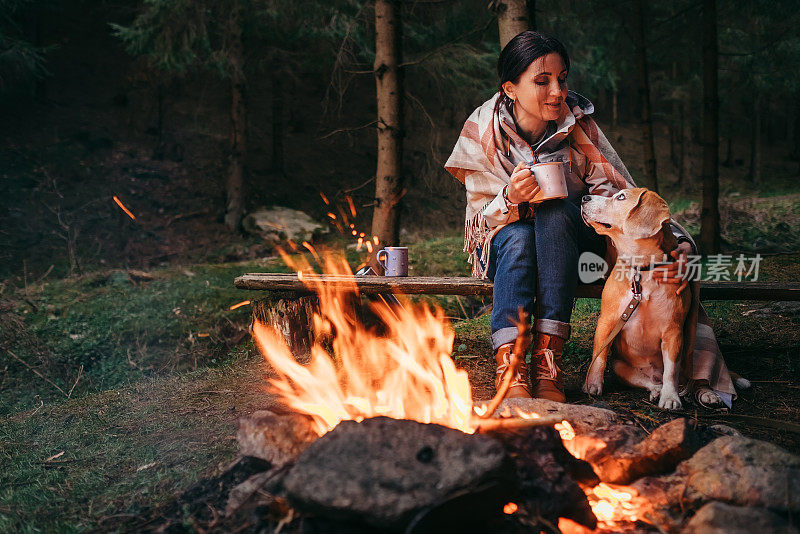 一个女人和一只小猎犬在篝火旁取暖