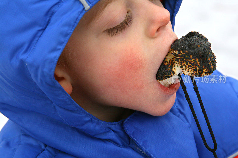 男孩在冬天吃烤棉花糖