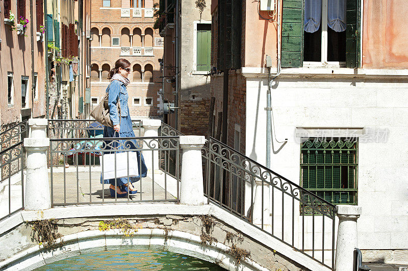 意大利威尼斯，一个女人拿着购物袋走过一座桥