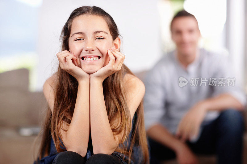 快乐的小女孩微笑着，她模糊的父亲在后面
