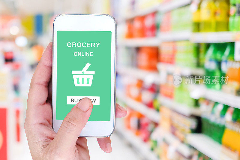 手持智能手机与杂货网上购物屏幕上模糊超市背景，零售业务和技术概念