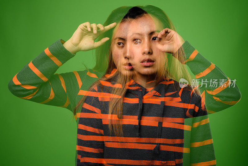 年轻的亚洲妇女与染头发穿着条纹帽衫对绿色的背景