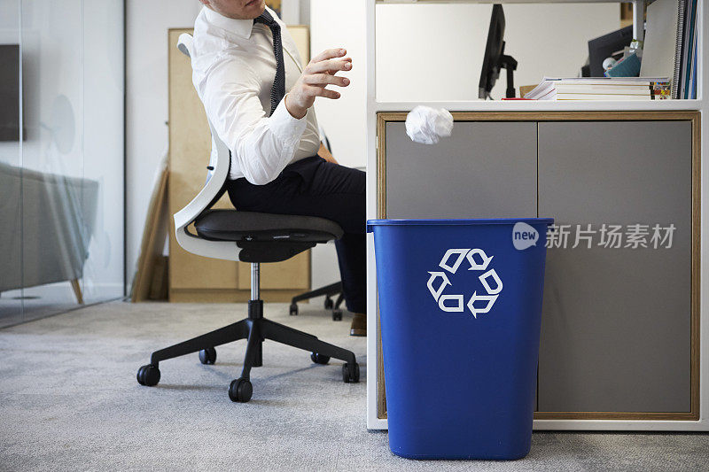 一个人在办公桌前把纸扔进回收箱