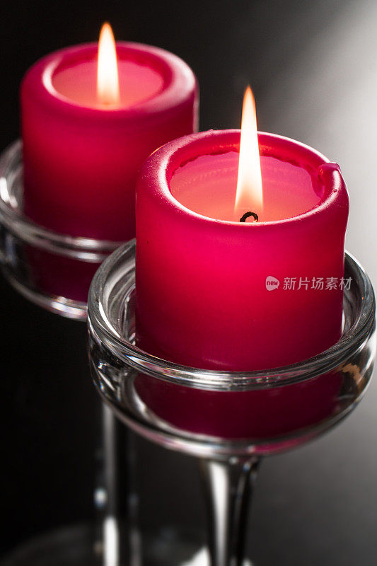 玻璃烛台上的两支红色蜡烛在黑色的背景下燃烧着