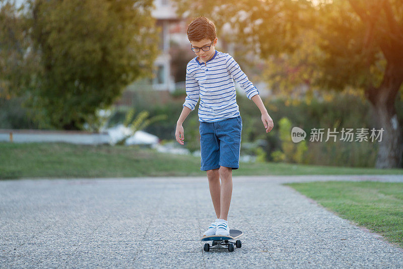 快乐的男孩在他的滑板上在公园咧嘴笑