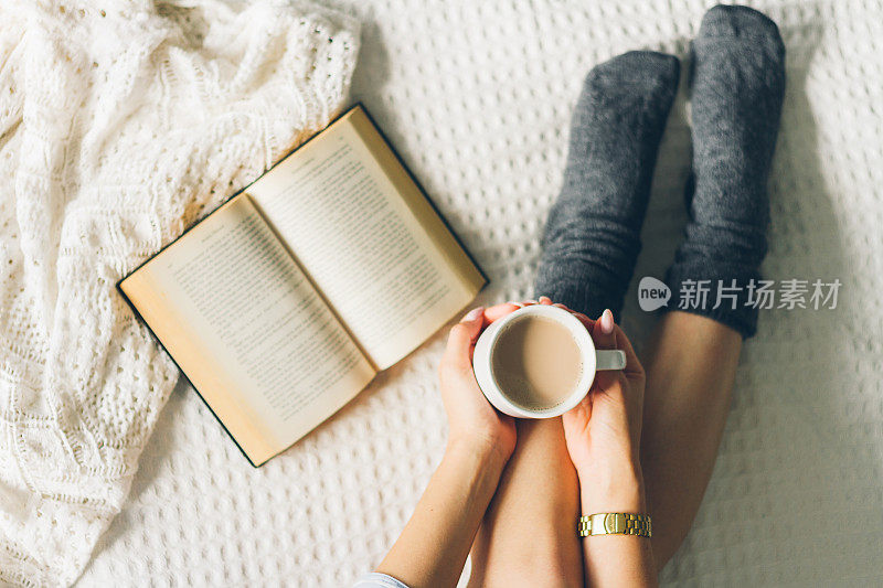 女人躺在床上，用一杯咖啡看书。