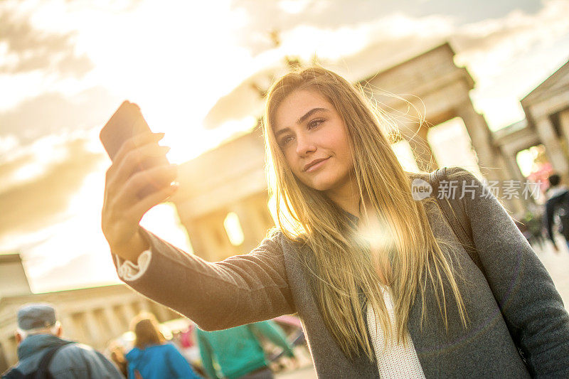 德国柏林市中心，一名年轻女子拿着智能手机自拍。