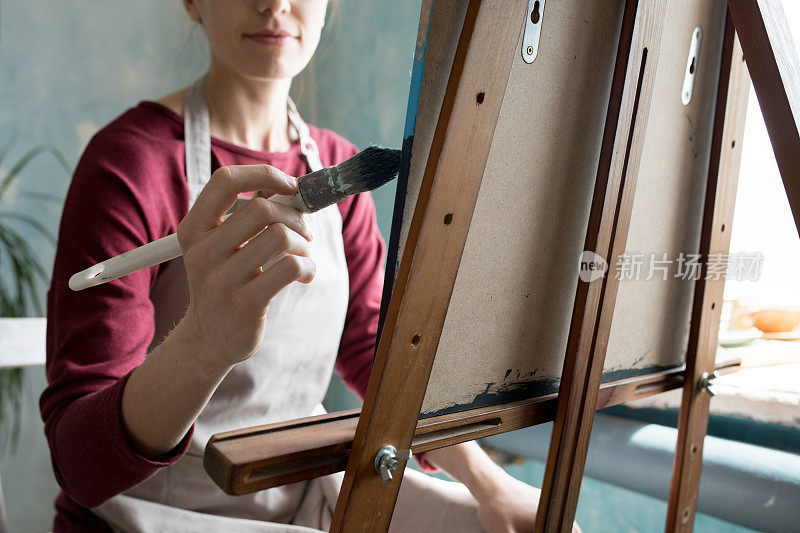 特写内容年轻女子在围裙绘画与画笔在画布上，而创造的图片在自己的工作室