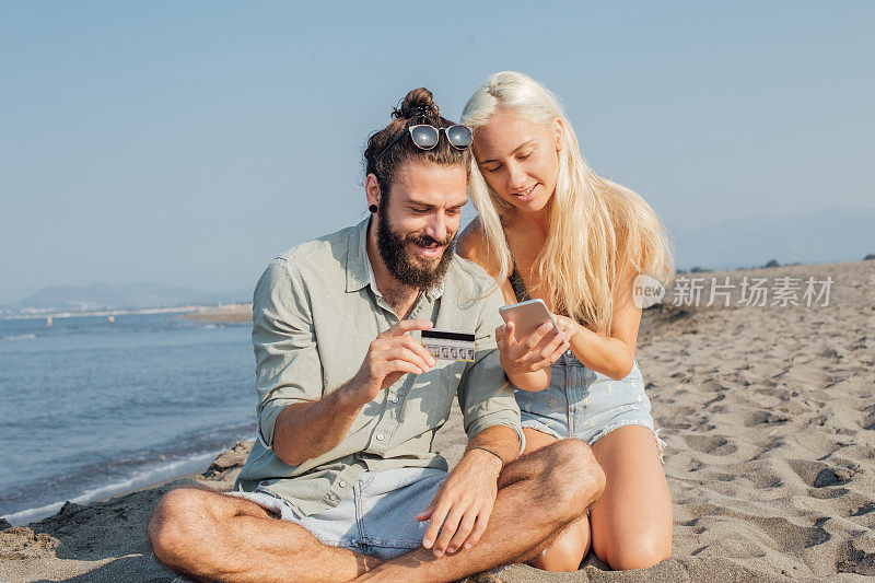 一对年轻夫妇在阳光明媚的海滩上做网上购物