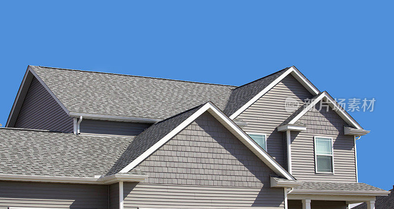 两层现代家庭显示屋顶，乙烯基壁板，和排水沟。背景是蓝色的天空。