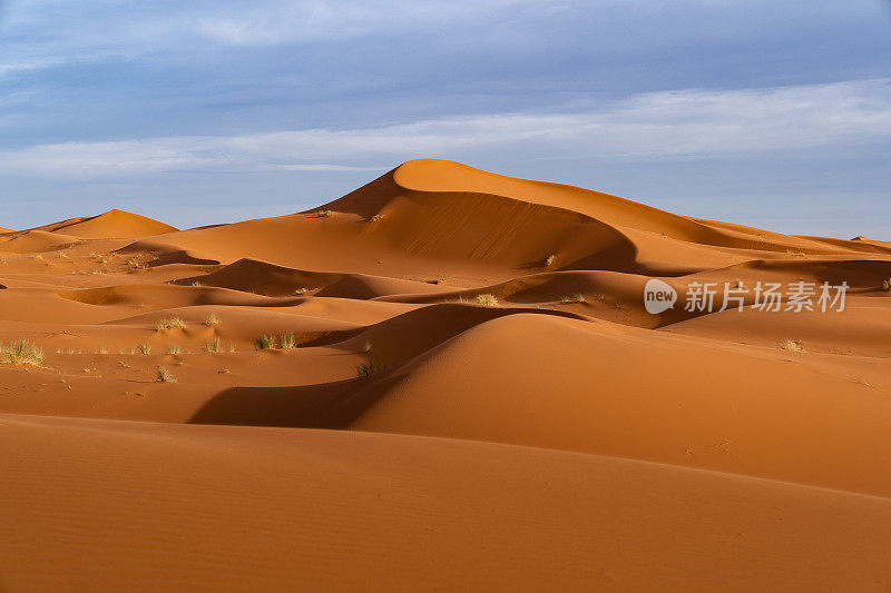 巨大的橙色沙状沙丘和多云的天空在Merzouga沙漠，摩洛哥。