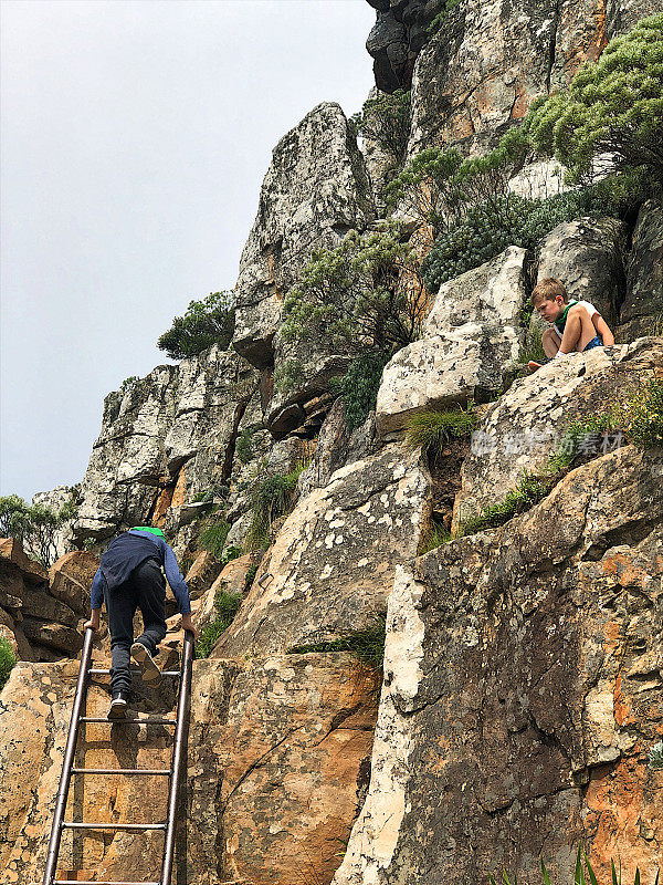 两个男孩在户外徒步旅行，爬上铁梯爬上岩壁