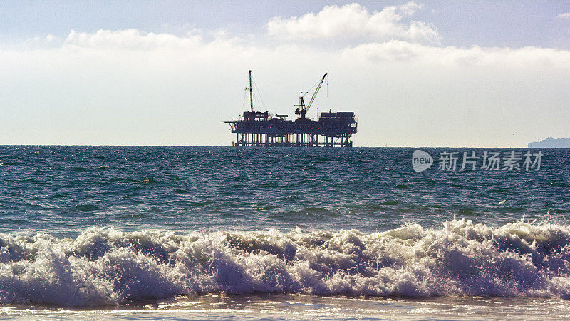 在一个阳光明媚的日子里，海浪冲刷着位于南加州亨廷顿海滩海岸的海上石油钻井平台