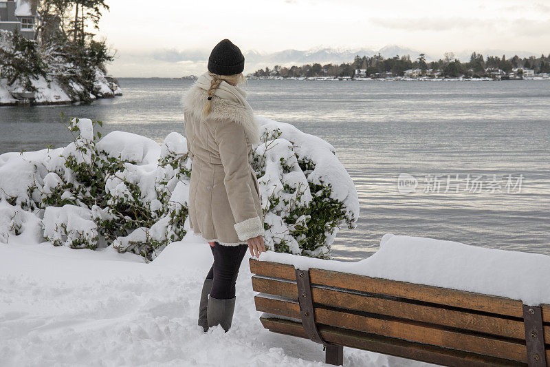 一个女人站在白雪覆盖的海岸线上望着海港