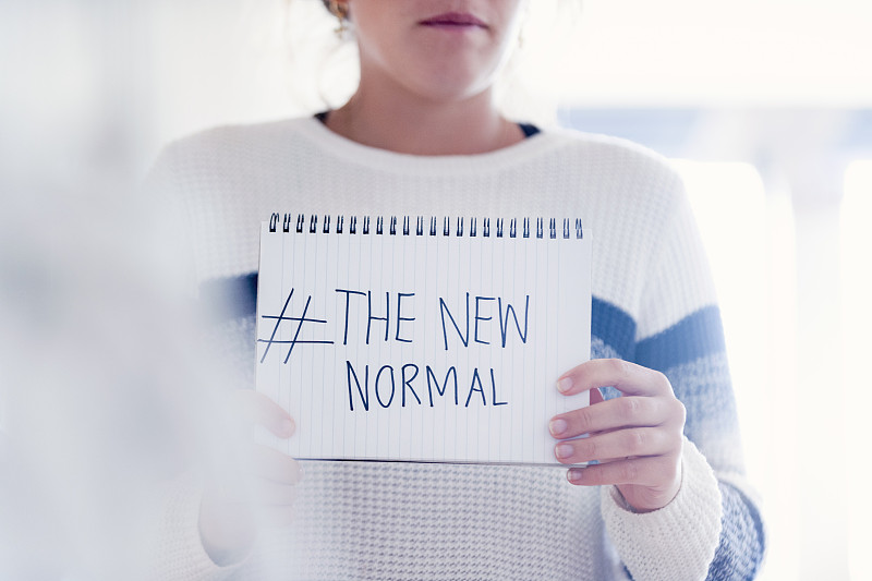 女人拿着写在便签本上的#新常态标志。说明了新常态的陈词滥调概念