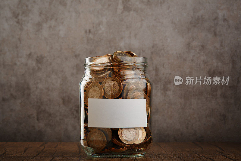 硬币储蓄罐与空白标签装满现金的桌子和水泥墙为背景