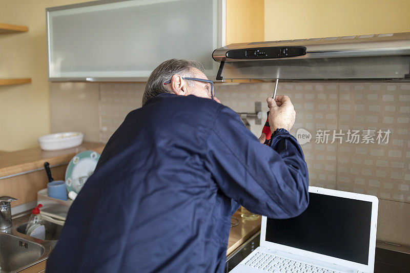 一位老年工人正在修理厨房里的排气过滤器。