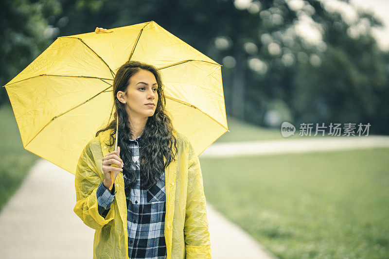 女人穿着雨衣，撑着雨伞，在雨天行走