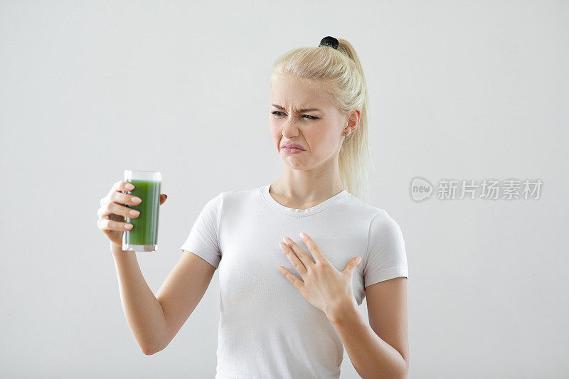 年轻女子拿着排毒绿汁，脸上带着愤怒的消极表情